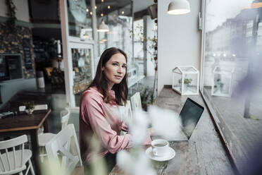 Confident female entrepreneur with laptop and coffee cup at table in cafe - JOSEF03153