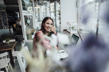 Happy female professional with laptop and coffee cup at table in cafe - JOSEF03154