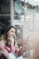Unternehmerin mit Hand am Kinn bei der Nutzung eines Smartphones in einem Café - JOSEF03159