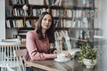 Businesswoman sitting with book at table in cafe - JOSEF03160