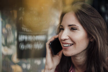 Weibliche Fachkraft lächelt, während sie in einem Café mit ihrem Smartphone telefoniert - JOSEF03165