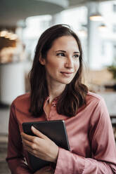 Lächelnde weibliche Fachkraft schaut weg, während sie ein digitales Tablet in einem Café hält - JOSEF03176