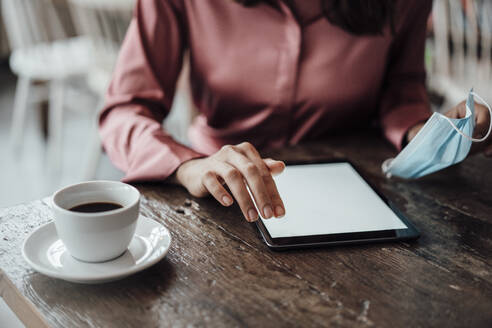 Businesswoman's hand using digital tablet at table in cafe during COVID-19 - JOSEF03180