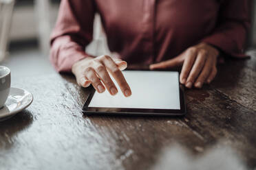 Businesswoman's hand using digital tablet at table in cafe - JOSEF03182