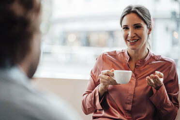 Eine lächelnde Geschäftsfrau trinkt Kaffee und diskutiert mit einem männlichen Kollegen in einem Café - JOSEF03188