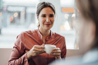 Eine Frau trinkt Kaffee und diskutiert mit einem männlichen Kollegen in einem Café - JOSEF03189