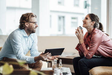 Male and female colleagues laughing while discussing in coffee shop - JOSEF03193