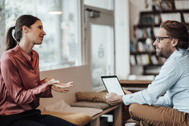 Unternehmerin diskutiert mit einem männlichen Kollegen über ein digitales Tablet in einem Café - JOSEF03199