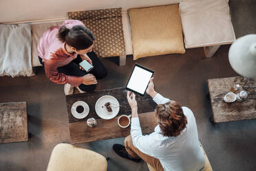 Weibliche und männliche Kollegen diskutieren in einem Café über ein digitales Tablet - JOSEF03200
