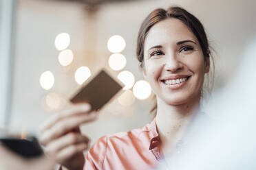 Smiling businesswoman holding credit card at cafe - JOSEF03217