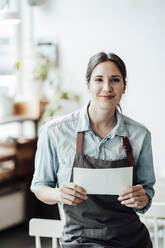 Smiling female owner holding paper at cafe - JOSEF03231