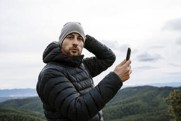 Männlicher Tourist am Aussichtspunkt, der sein Smartphone im Winter gegen den Himmel hält - AFVF08123