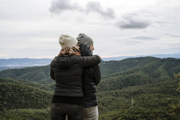 Touristisches Paar, das sich umarmt und wegschaut, während es an einem Aussichtspunkt steht - AFVF08126