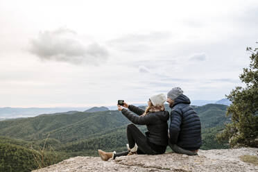 Couple taking selfie while sitting on observation point against sky - AFVF08134