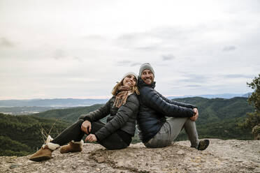 Lächelndes Paar sitzt Rücken an Rücken auf dem Aussichtspunkt gegen den Himmel - AFVF08138