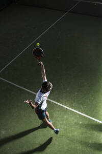 Male athlete servicing ball while playing padel tennis in sports court at night - DAMF00671