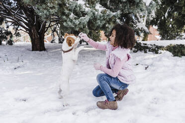 Cute girl playing with dog in snow at park - EBBF02306