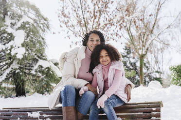 Mother and daughter sitting on bench in park - EBBF02307