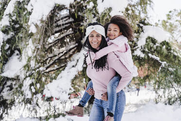 Happy mother giving piggyback ride to daughter in park - EBBF02314