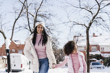 Mother and daughter holding hands while walking on street during winter - EBBF02318