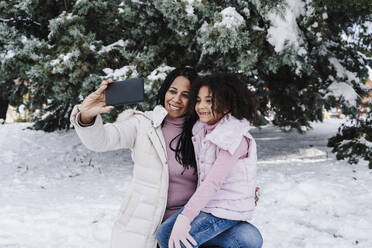 Happy mother and daughter taking selfie on smart phone in park - EBBF02319