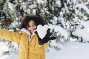 Nettes Mädchen zeigt herzförmigen Schnee, während sie im Park steht - EBBF02326