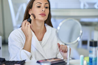 Woman applying blusher while looking in mirror at home - KIJF03522