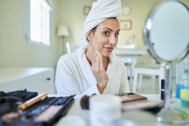 Smiling woman removing make-up in living room at home - KIJF03539