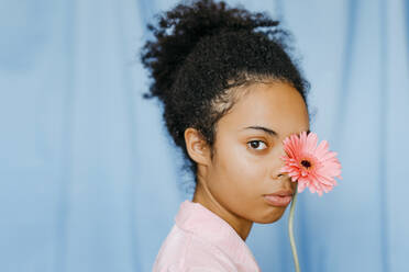 Lockenköpfige Frau bedeckt Auge mit rosa Gerbera-Gänseblümchen - TCEF01516