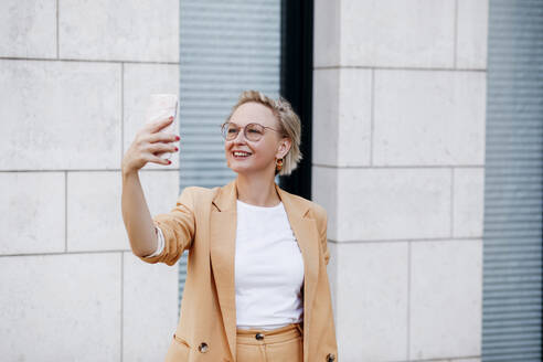 Lächelnd reifen weiblichen professionellen Aufnahme selfie durch Smartphone gegen Wand - KMKF01488
