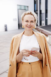 Smiling beautiful businesswoman with smart phone - KMKF01496