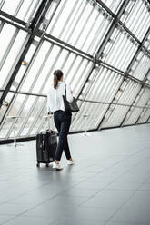 Female entrepreneur with suitcase walking in corridor of office - JOSEF03258