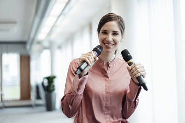 Smiling businesswoman singing through microphone in office - JOSEF03263