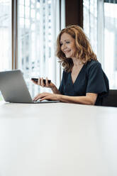 Senior businesswoman working on laptop at table in office - JOSEF03279