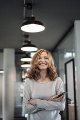 Smiling senior businesswoman with smart phone in illuminated office - JOSEF03340