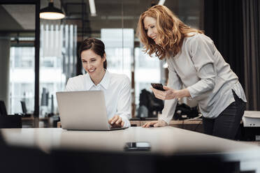 Smiling businesswoman discussing over laptop at conference table in board room - JOSEF03357