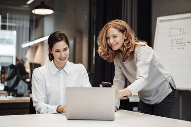 Happy businesswoman discussing with female colleague at conference table during meeting in office - JOSEF03359