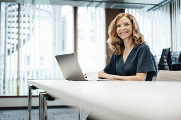 Smiling businesswoman with laptop at conference table in board room at office - JOSEF03367