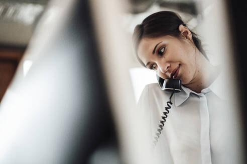 Female entrepreneur talking on landline phone at office - JOSEF03396