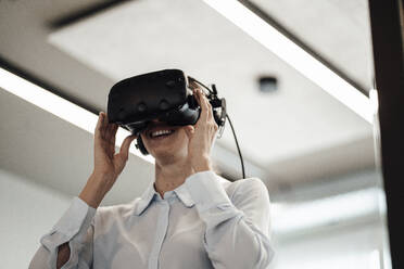 Smiling female entrepreneur wearing virtual reality simulator at office - JOSEF03406