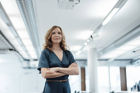 Confident businesswoman with arms crossed in illuminated office stock photo