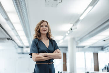 Confident businesswoman with arms crossed in illuminated office - JOSEF03424