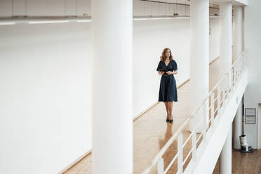 Female entrepreneur with digital tablet walking in corridor - JOSEF03434