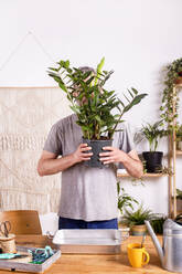 Mann hält Zamioculcas Zamiifolia Pflanze Blumentopf, während stehend durch Tabelle zu Hause - RTBF01515