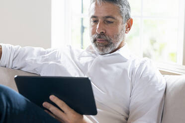 Businessman using digital tablet while sitting on sofa at home - SBOF02541