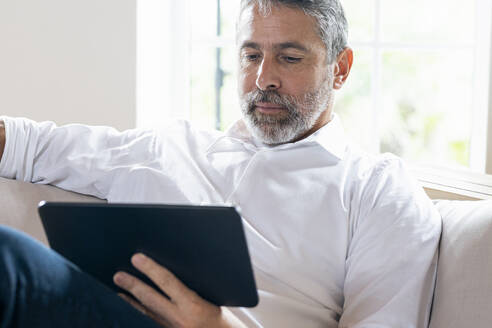 Geschäftsmann, der ein digitales Tablet benutzt, während er zu Hause auf dem Sofa sitzt - SBOF02541