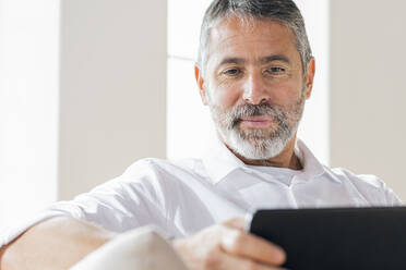 Älterer Geschäftsmann, der zu Hause sitzend ein digitales Tablet benutzt - SBOF02542