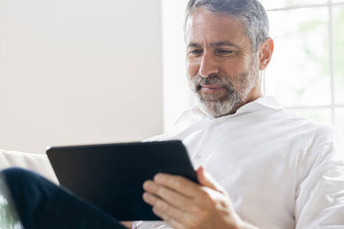 Lächelnder Geschäftsmann, der zu Hause sitzend an einem digitalen Tablet arbeitet - SBOF02552