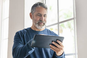 Lächelnder Geschäftsmann, der im Stehen zu Hause an einem digitalen Tablet arbeitet - SBOF02566