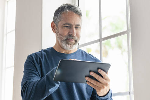 Lächelnder Geschäftsmann, der im Stehen zu Hause an einem digitalen Tablet arbeitet - SBOF02566